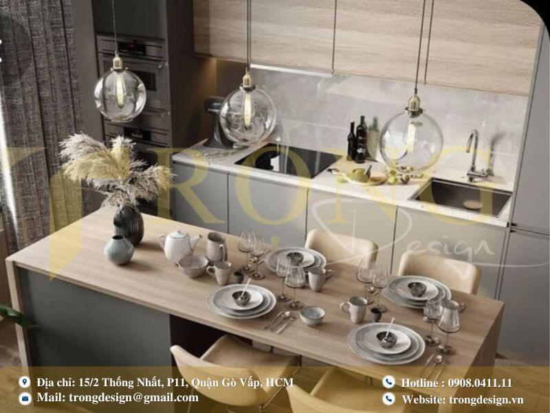 Bếp hiện đại với tủ bếp trắng gỗ sáng màu, đảo bếp liền bàn ăn và đèn thả.